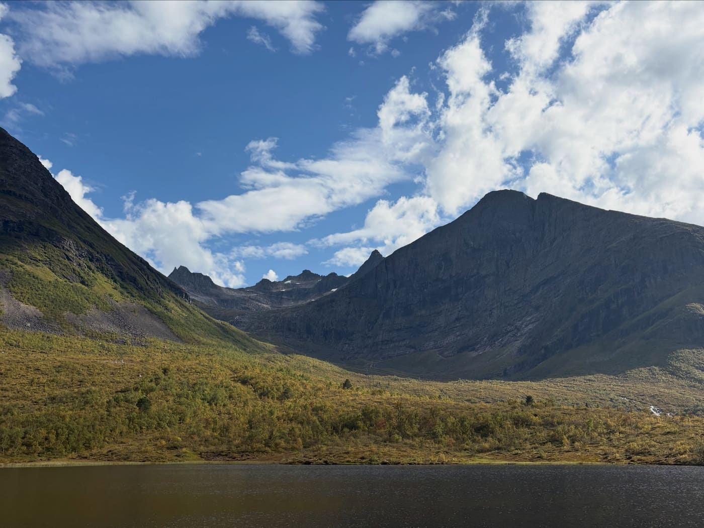 A broad mountain valley under a bright blue sky with scattered cloud