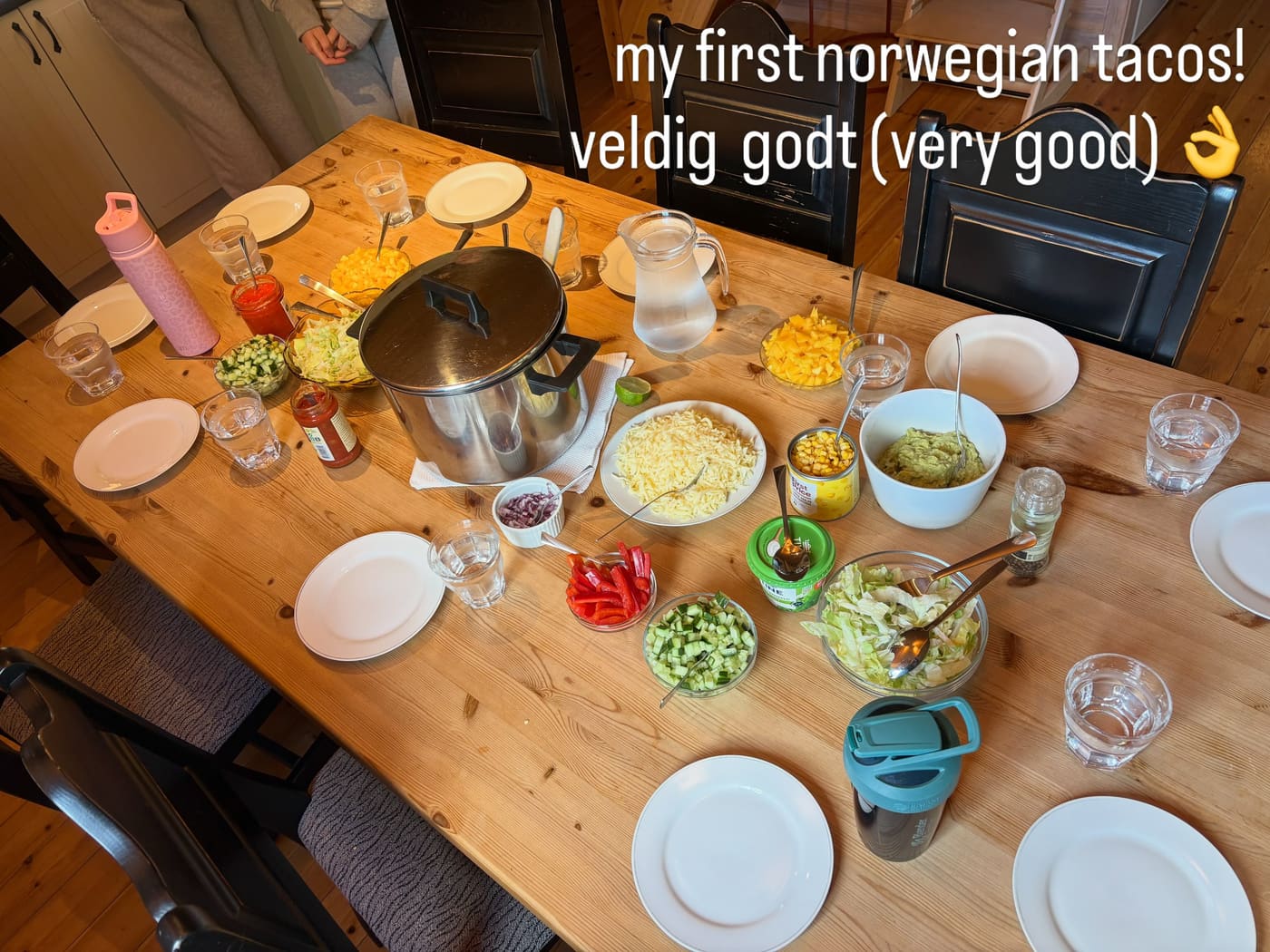 A long wooden table laid with bowls of taco fillings and glasses
