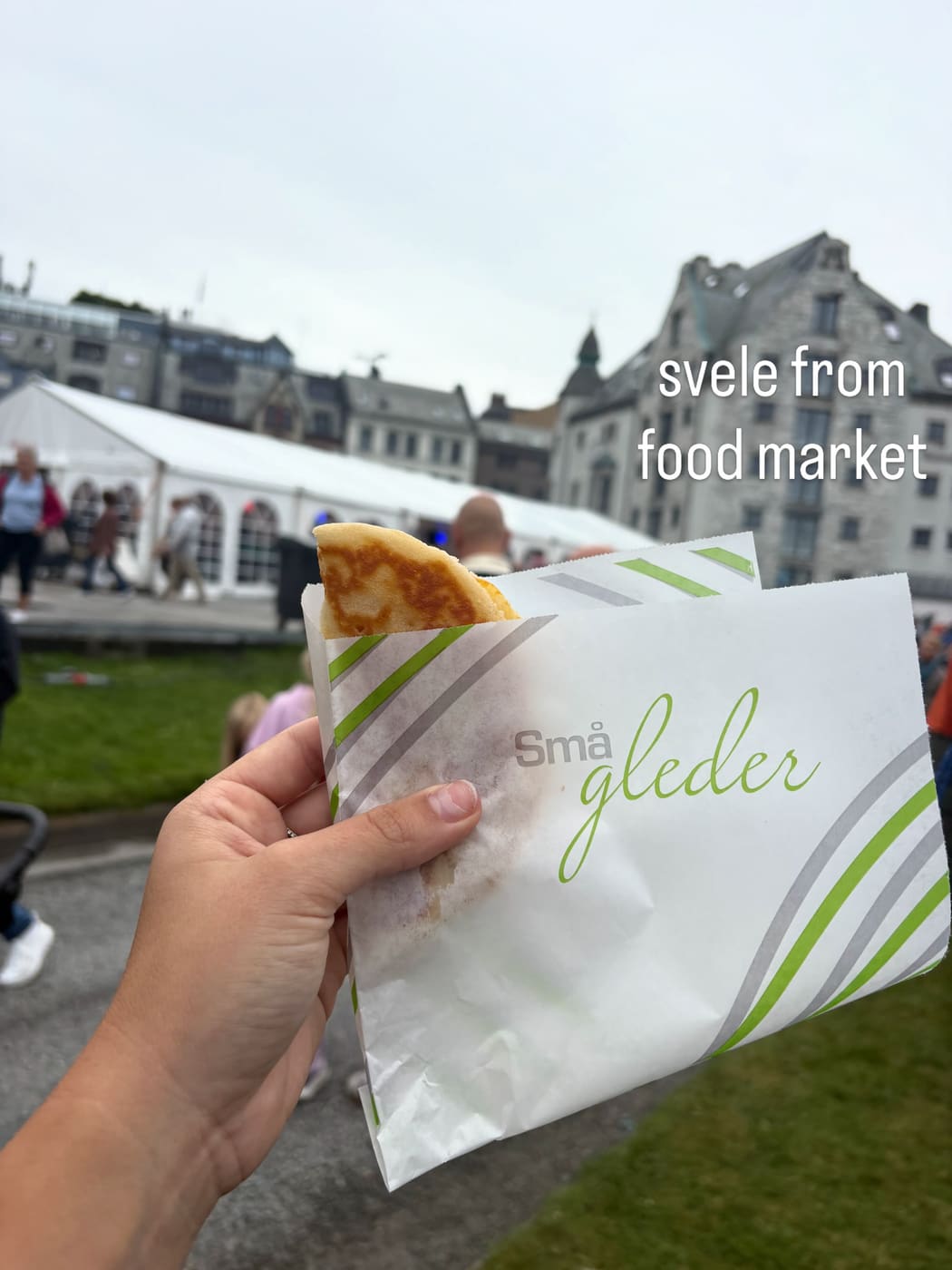 A hand holding a svele, a folded Norwegian pancake, in a paper wrapper at an outdoor market
