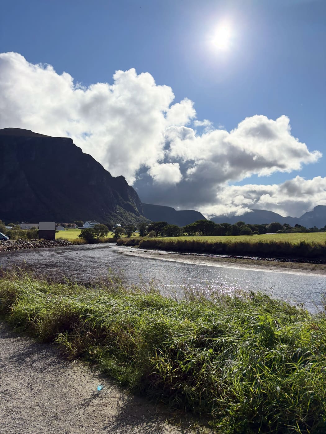 A wide green valley with a river winding through it, farm buildings and mountains behind