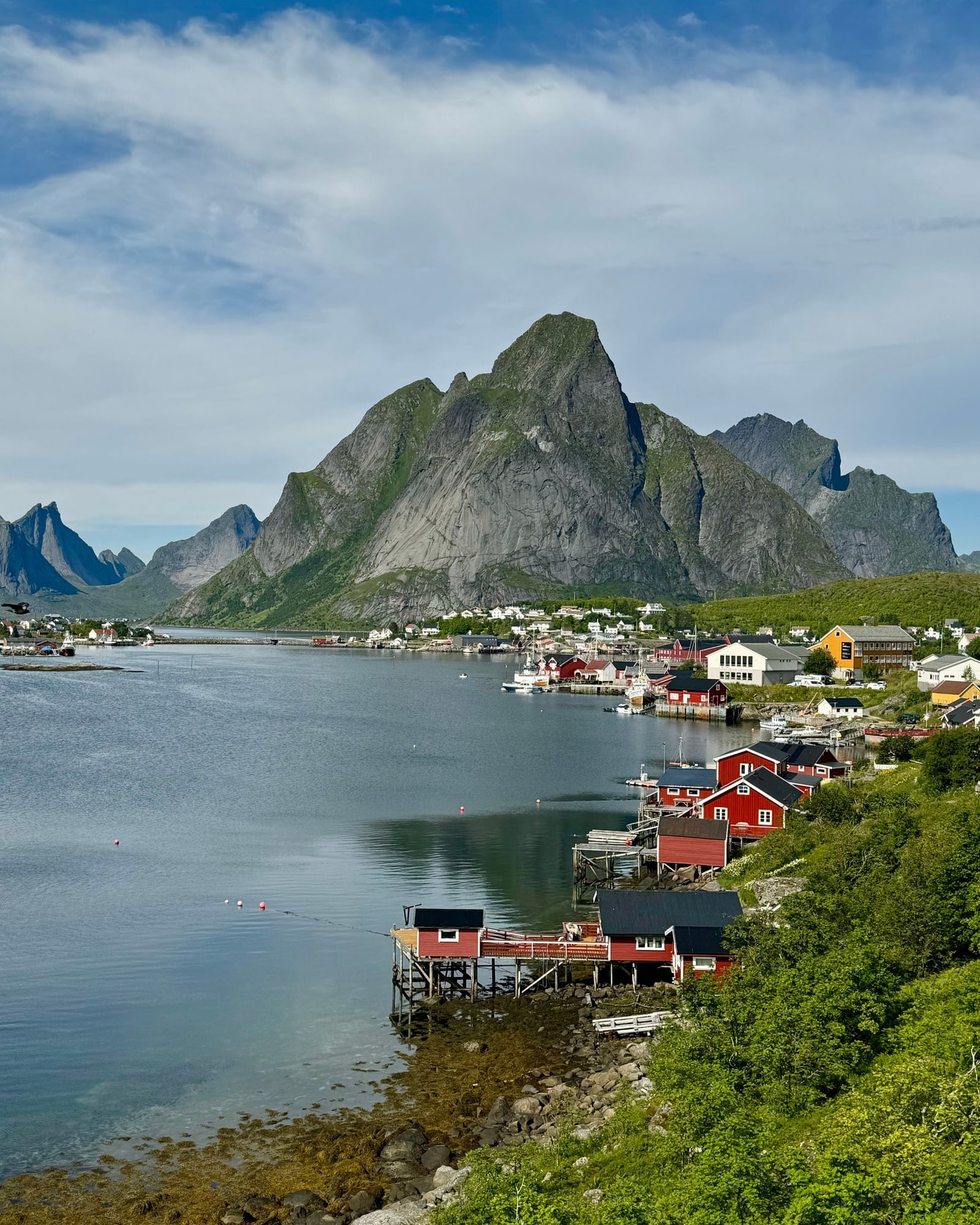 The village of Reine in Lofoten, red fishing cabins along the water below a steep grey mountain